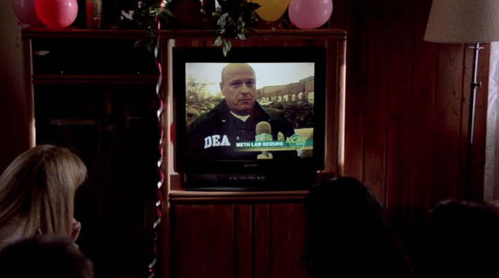 Guests at Walt’s 50th birthday party watch his brother-in-law Hank Schrader (Dean Norris) discuss a meth lab bust on TV