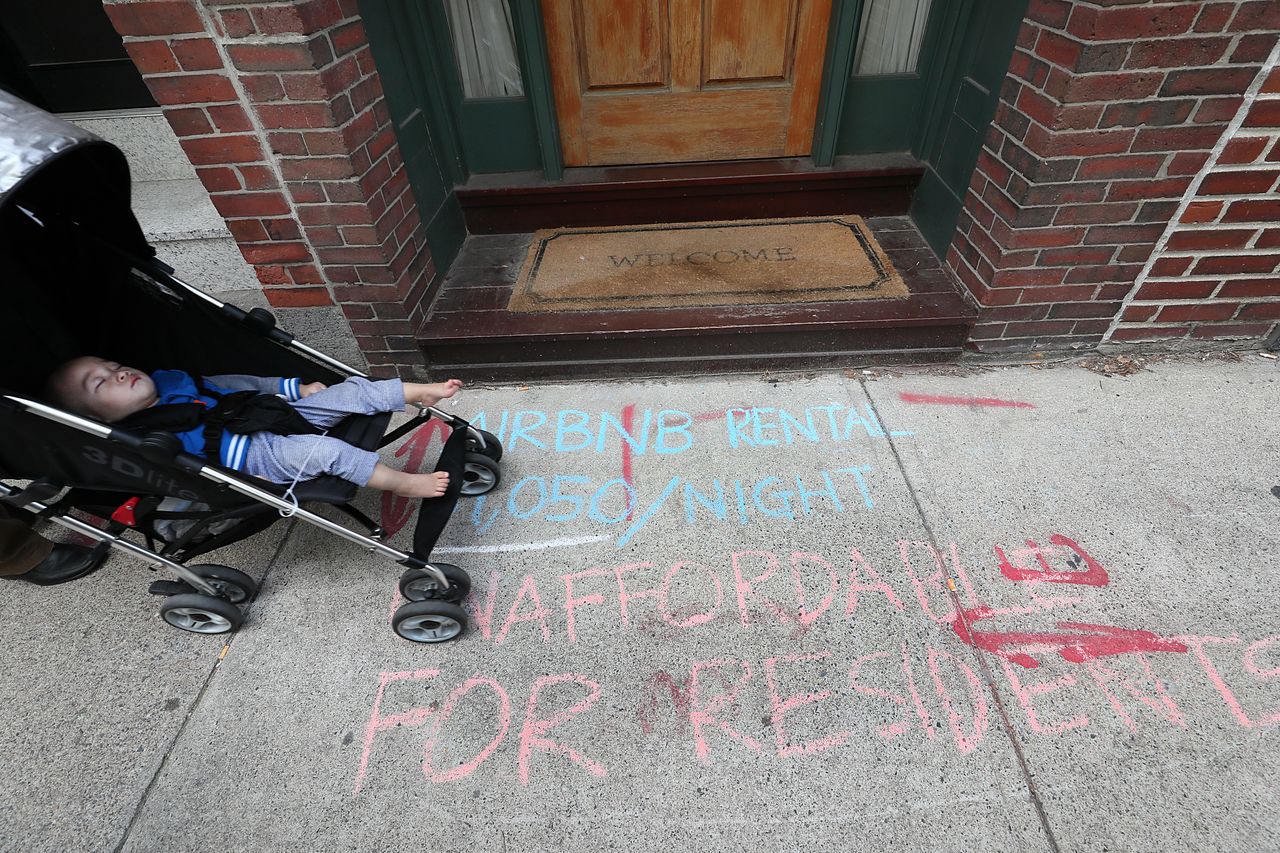 A family walks along Oak Street in Boston's Chinatown, where protestors for affordable housing have written on the sidewalk in front of an Airbnb rental.