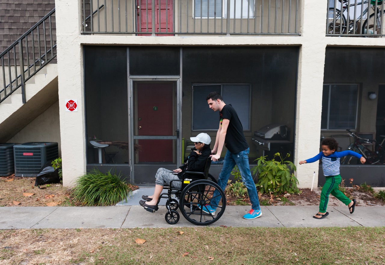 Jan Miguel pushes his mother, Mariluz, in a wheelchair on their way to get a ride to a doctor appointment. Jan Miguel’s cousin Emiliano follows closely.