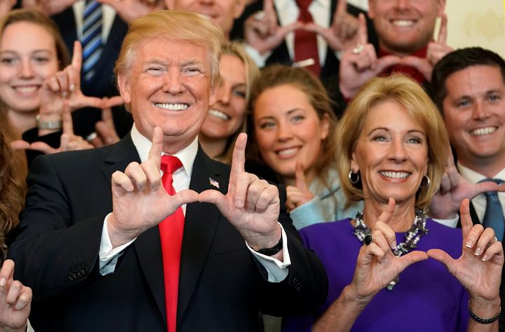 President Donald Trump and Education Secretary Betsy DeVos make "U" symbols with their hands while posing with the Utah Skiing team at the White House, Nov. 17, 2017.