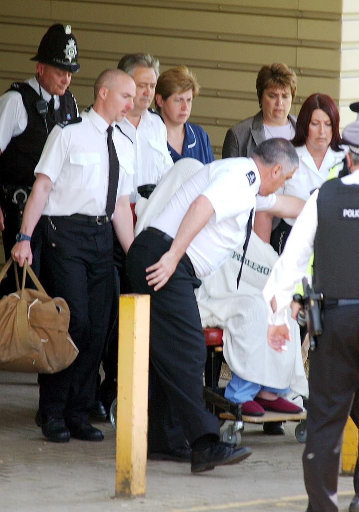 Huntley, hidden under a blanket and wearing blue pyjamas and red slippers is escorted from hospital to a van by police after a suicide attempt in 2003 