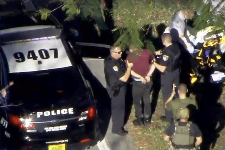 A man placed in handcuffs is led by police near Marjory Stoneman Douglas High School following a shooting incident in Parkland, Florida