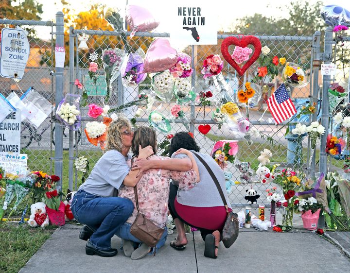 Shari Unger kisses Melissa Goldsmith as Giulianna Cerbono lights candles at a memorial at Marjory Stoneman Douglas High School where a gunman killed 17 students on February 14