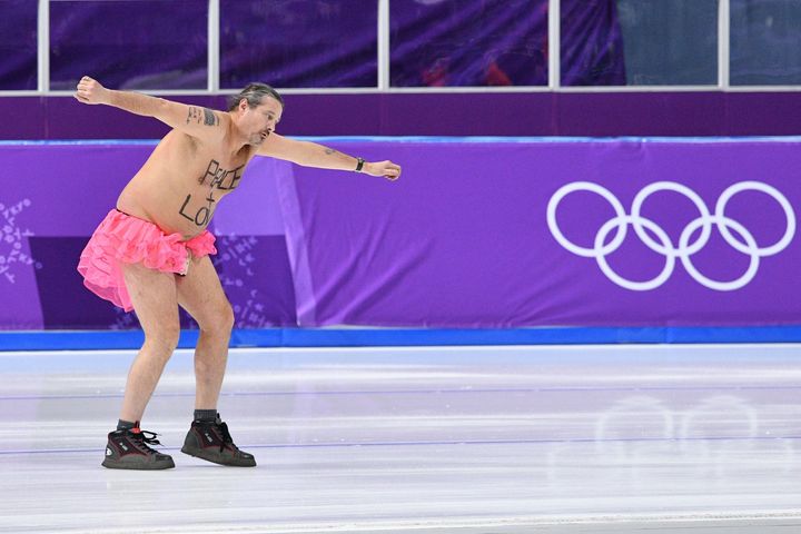 A shirtless man clad in a tutu dances on the rink following the men's 1,000 m speedskating medal ceremony.