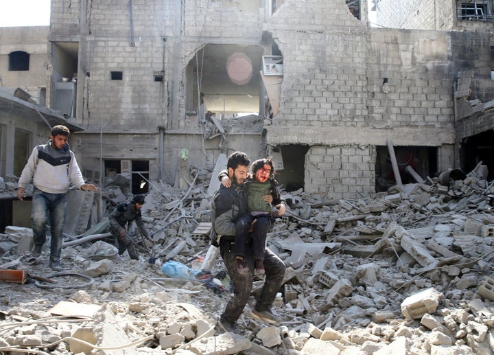 A man carries an injured boy as he walks on rubble of damaged buildings in the rebel held besieged town of Hamouriyeh, easter