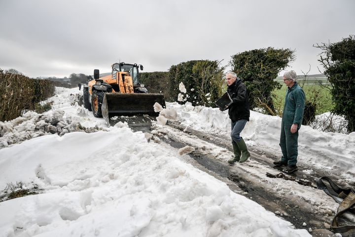A JCB machine arrives and scrapes the road surface to try free a lorry stuck in snow near Marlborough, Wiltshire