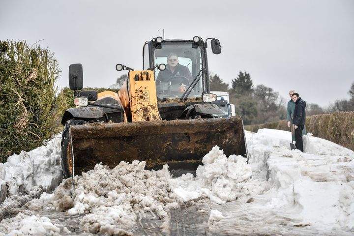 A JCB is used to scrape the road surface and clear snow after vehicles became stuck in snow near Marlborough, Wiltshire.