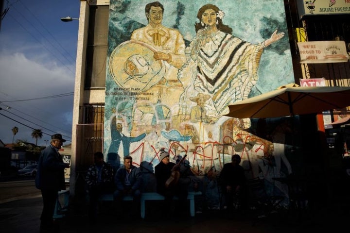 Men sit outside a store in front of the mural “El Corrido de Ricardo Valdez,” painted in 1994 by Juan Solis, in Mariachi Plaza in February in Boyle Heights, Los Angeles. 