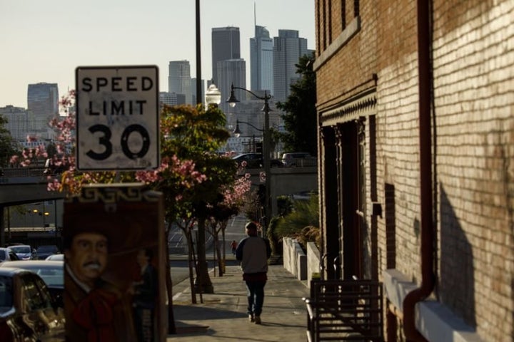 A pedestrian walks near Mariachi Plaza in Boyle Heights with the skyline of downtown Los Angeles on the horizon. 