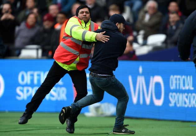 A pitch invader is confronted by security during the Premier League match at the London Stadium.