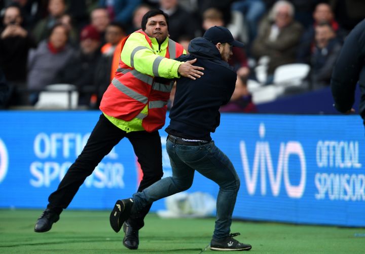 A pitch invader is confronted by security during the Premier League match at the London Stadium.