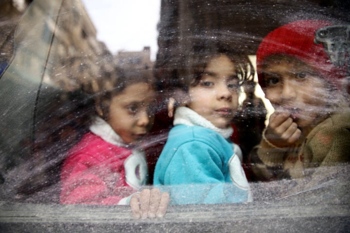 Children look through a bus window during an evacuation from the besieged town of Douma, in Syria's eastern Ghouta region, on March 13, 2018. 