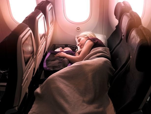 A parent lying down with a baby in an infant pod on an Air New Zealand flight.