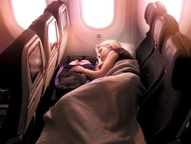 A parent lying down with a baby in an infant pod on an Air New Zealand flight. 