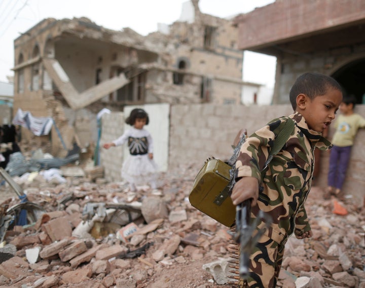 A boy carries a toy gun next to destroyed houses on June 21, 2016, during a vigil marking a year since a Saudi-led airstrike on a residential area in Sanaa, Yemen.