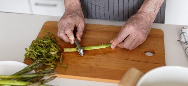 Lay raw asparagus on a cutting board and peel away rough bits with a vegetable peeler.