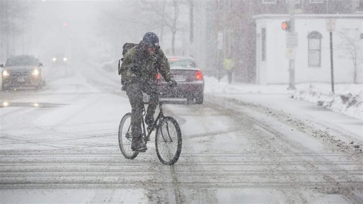 <p>A bicyclist crosses the street in Portland, Maine, this month as heavy snow begins to fall. Several states are considering bills that would allow bicyclists to treat red lights as stop signs and stop signs as yield signs.</p>