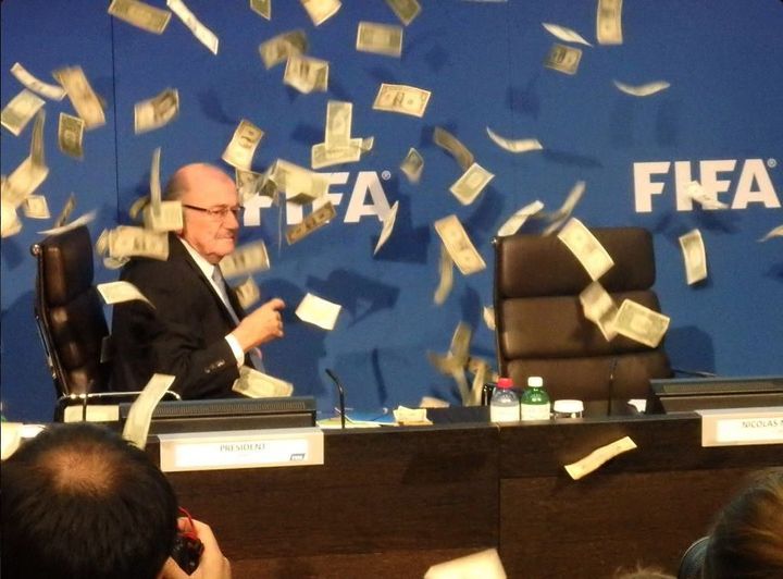 Sepp Blatter surrounded by cash thrown at him by comedian Simon Brodkin