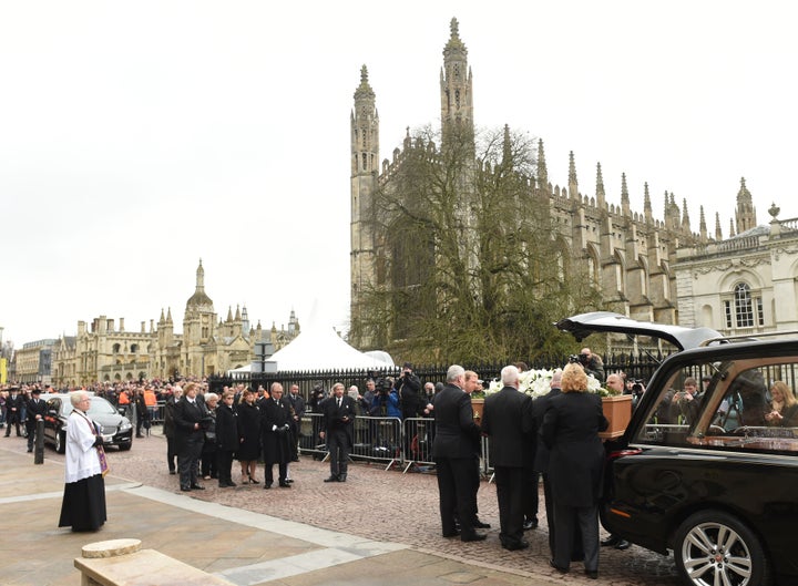 Relatives and family members wait as the coffin is lifted from the hearse