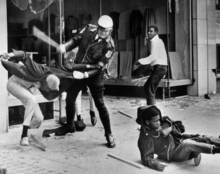 A police officer uses his nightstick on a youth reportedly involved in the looting that followed the breakup of a march led b