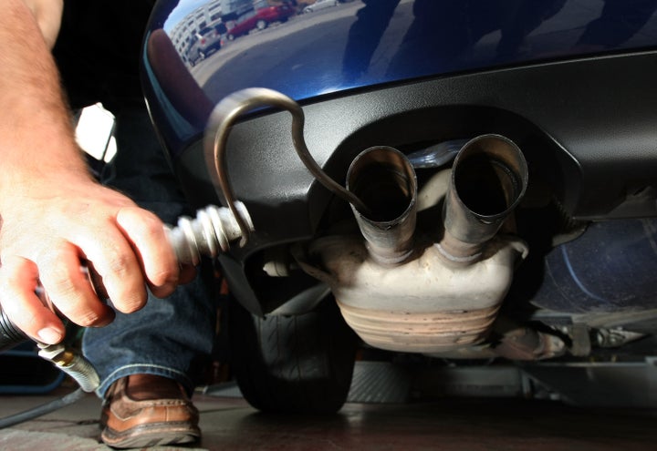 A man in California inserts a probe into the tailpipe of a car while performing an emission test. 