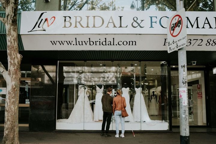 Agnew, who is using her cane, and her brother Cal gaze into the window of the bridal shop where four white gowns are displayed on mannequins.