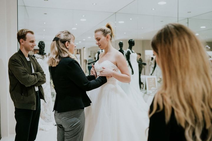 Agnew guides her mom's hands to the fitted bodice of a strapless gown while her brother and the bridal consultant look on.