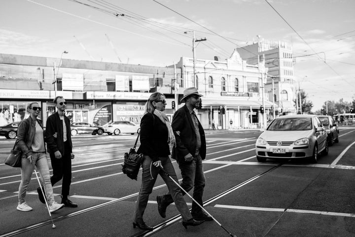 Agnew, left, walks arm-in-arm with her brother Cal as they cross the street. Ahead of them are their parents, who also walking arm-in-arm, as cars wait for them to pass. Both Agnew and her mother have cone-rod dystrophy and are using canes.