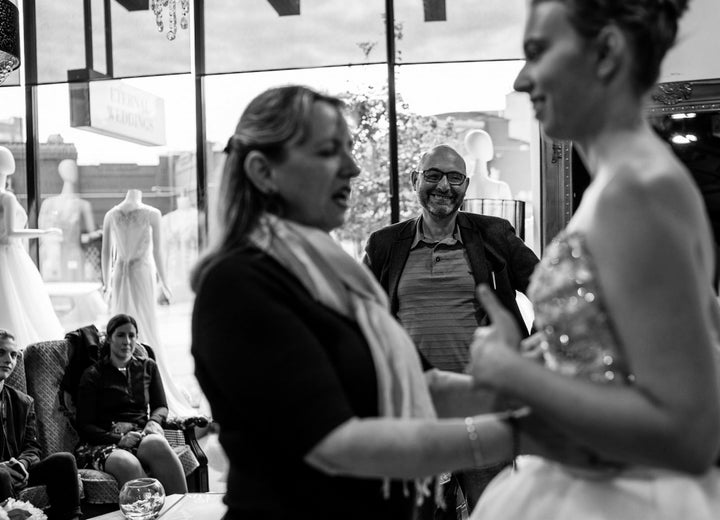 Agnew's mom touches the bodice of the beaded wedding dress her daughter has tried on. The father of the bride stands behind them, looking on with his hands on his hips and a proud smile on his face.