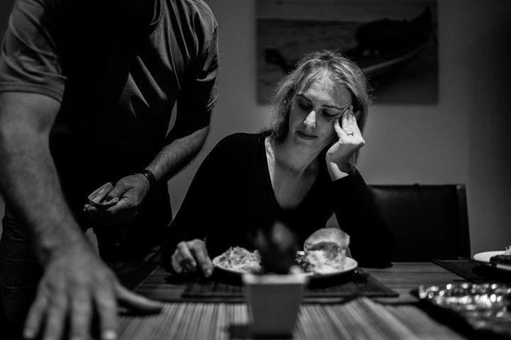 In this black-and-white photo, Campbell leans over Agnew as he sets the dining room table for dinner. Agnew has a plate of food in front of her with a bread roll on the right and salad on the left.