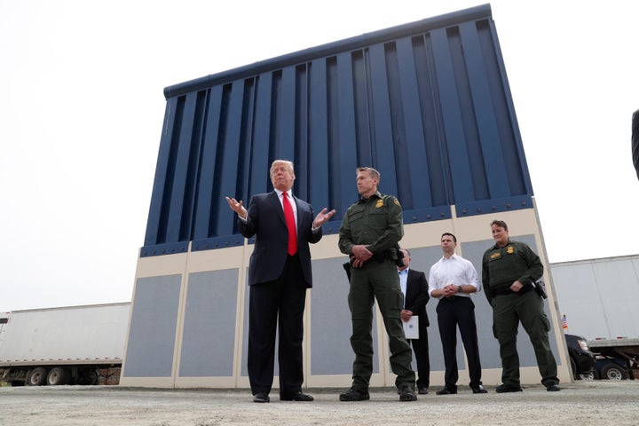President Donald Trump stands with a Customs and Border Protection agent in front of a border wall prototype while visiting S