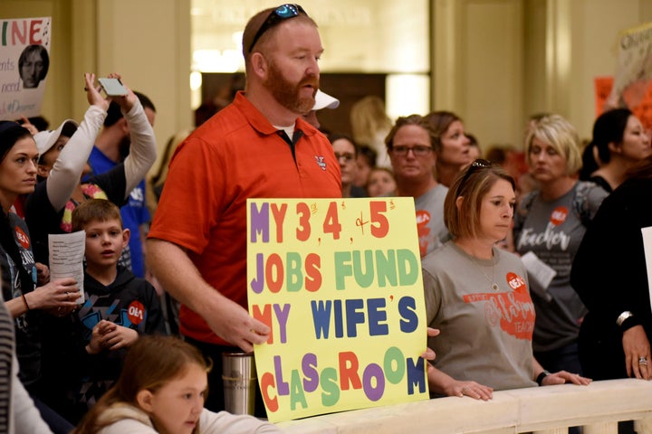 A supporter holds a sign that reads "My 3rd, 4th, and 5th jobs fund my wife's classroom" inside the Oklahoma Capitol on the second day of a teacher walkout.