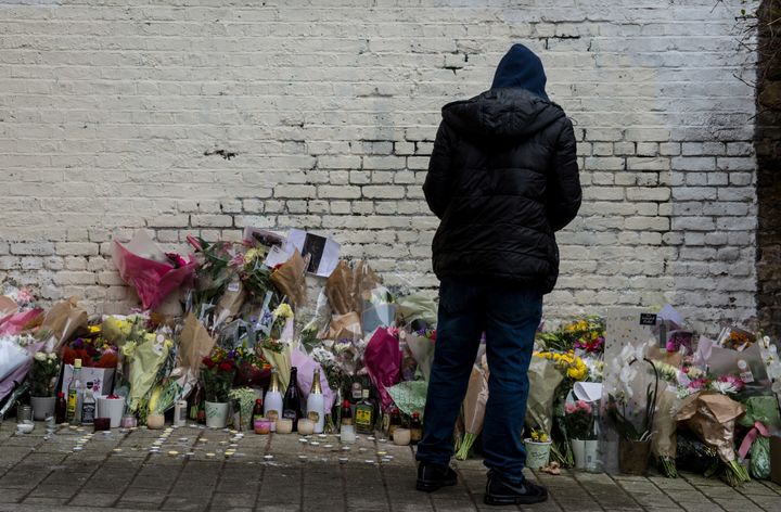 A young man looks at messages and flowers left at the scene in Hackney