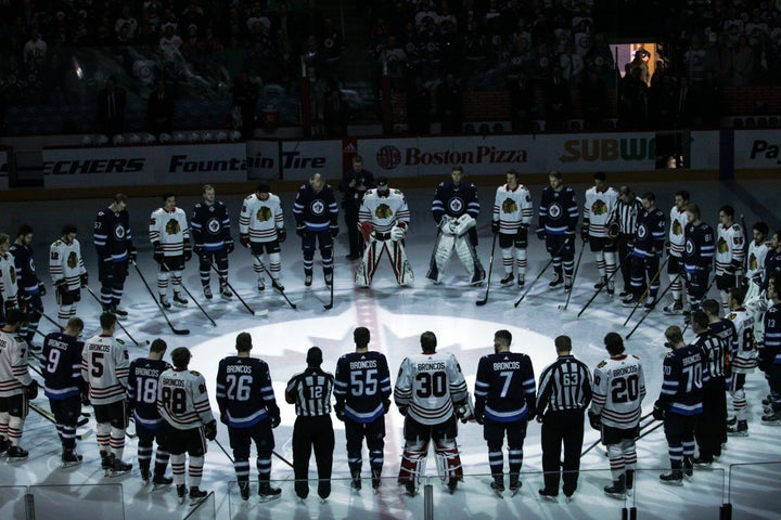 The Winnipeg Jets and Chicago Blackhawks, wearing jerseys reading "Broncos" on their backs, observe a minute of silence