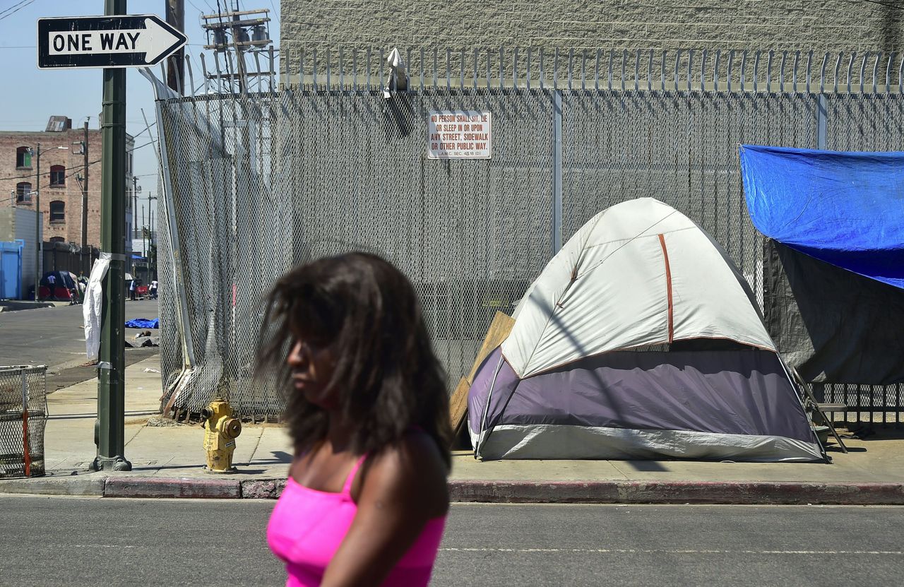 A woman walks past a sign posting the ordinance that led to the explosion of tents housing the homeless on Los Angeles streets near Skid Row. 