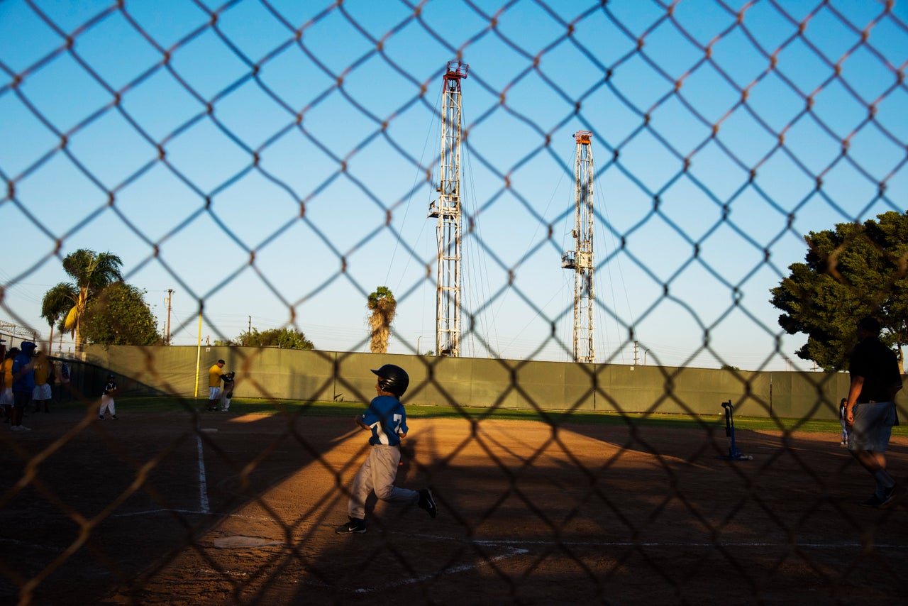 Two oil rigs loom over an April 16 coach-pitch game at the John Mendez Baseball Park in Wilmington.