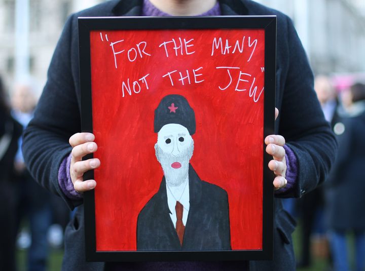 A demonstrator holding a painting saying "For the many not the Jew", as people protest against anti-Semitism in the Labour party in Parliament Square