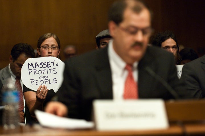 A protester holds a sign behind Don Blankenship, who had been chairman and CEO of Massey Energy Co. until a deadly explosion at one of his mines killed 29 people.