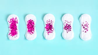 Menstrual pad with bright purple glitter on blue colored background. Woman periods cycle, menstruation frequency. Minimalist still life photography concept