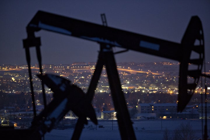 City lights are seen at night as pumpjack operates above an oil well in the Bakken Formation on the outskirts of Williston, North Dakota.