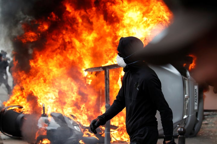 A masked demonstrator walks near a car that burns outside a Renault automobile garage in Paris during May Day protests.