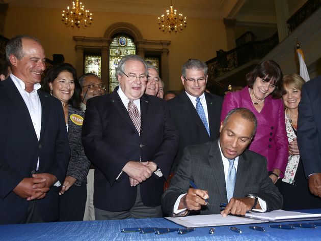 Deval Patrick, former governor of Massachusetts, signs a 2014 gun violence bill while Robert DeLeo, the House Speaker, looks