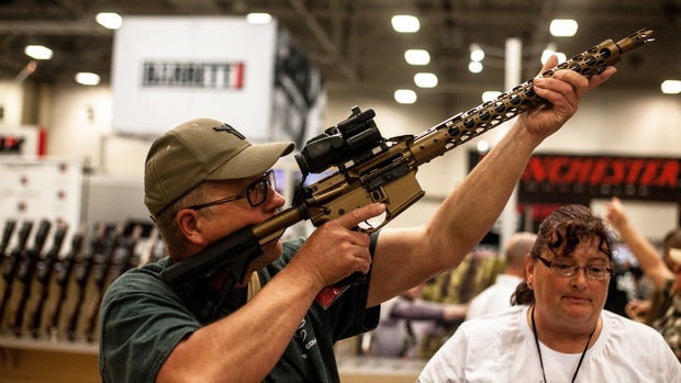Tim Oelklaus of Missouri holds up a display rifle on the expo floor of the annual NRA meeting in Dallas, TX on May 4, 2018.