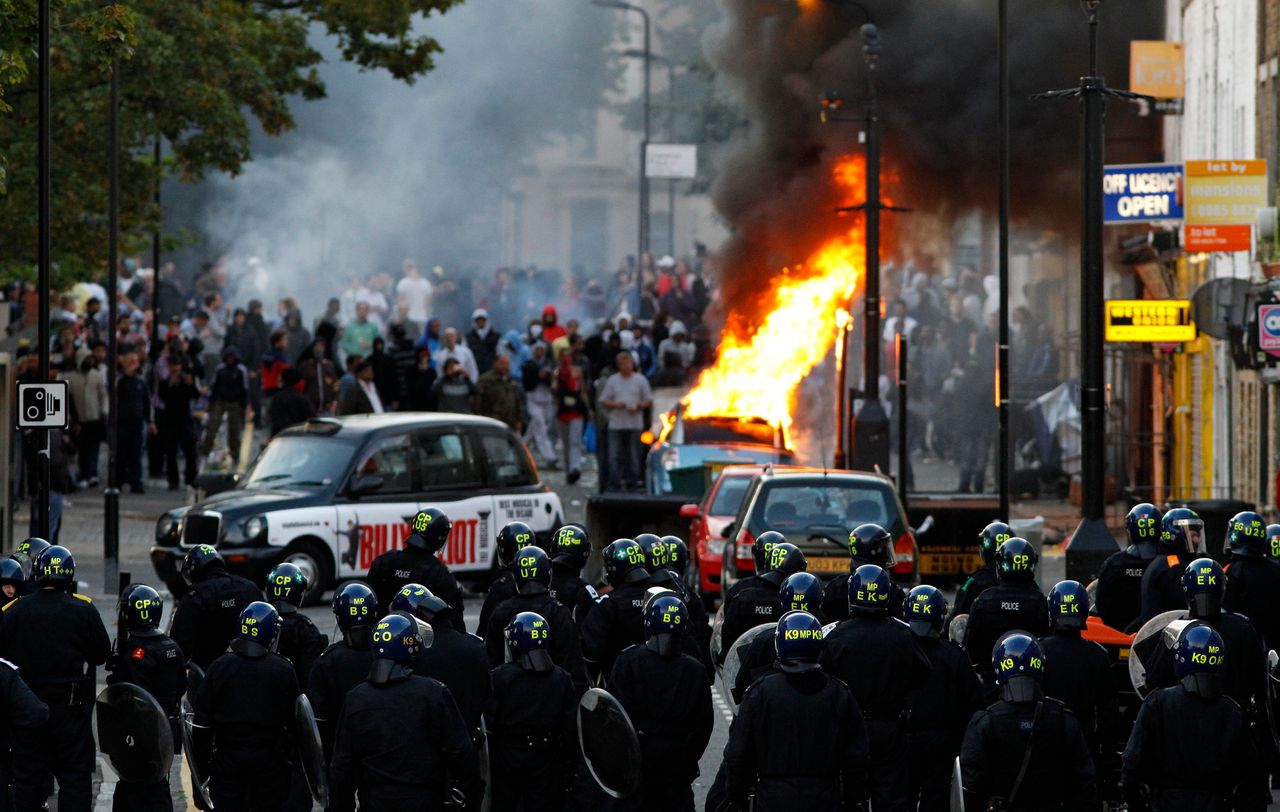 Police officers in riot gear block a road near a burning car on a street in Hackney, east London August 8, 2011.