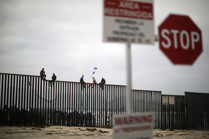 Members of a migrant caravan from Central America and their supporters sit on the top of the U.S.-Mexico border wall at Border Field State Park before making an asylum request.