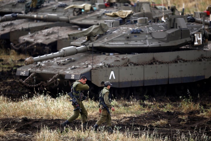 Israeli soldiers walk next to tanks near the Israeli side of the border with Syria in the Israeli-occupied Golan Heights, Isr