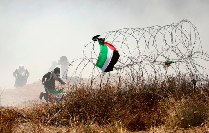 A Palestinian protester holding his national flag runs past barbed wires during clashes with Israeli forces near the border b