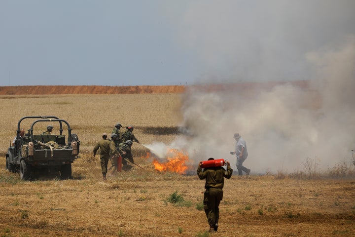 Israeli soldiers attempt to extinguish a fire in a field on the Israeli side of the border fence between Israel and Gaza near