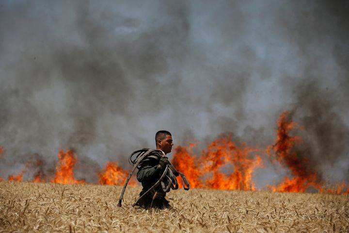 An Israeli soldier carries a hose as he walks in a burning field on the Israeli side of the border fence between Israel and Gaza near kibbutz Mefalsim.