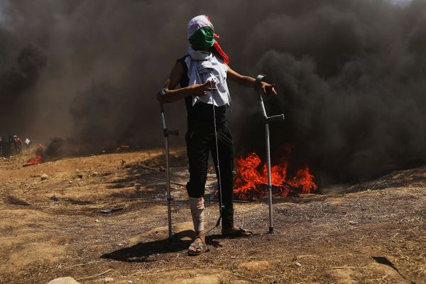 A wounded Palestinian protestor stands at the border fence. 